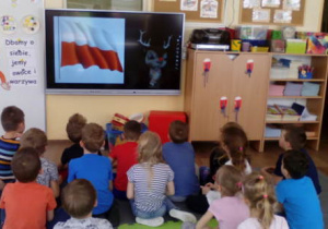 Dzieci siedząc oglądają prezentację multimedialną.